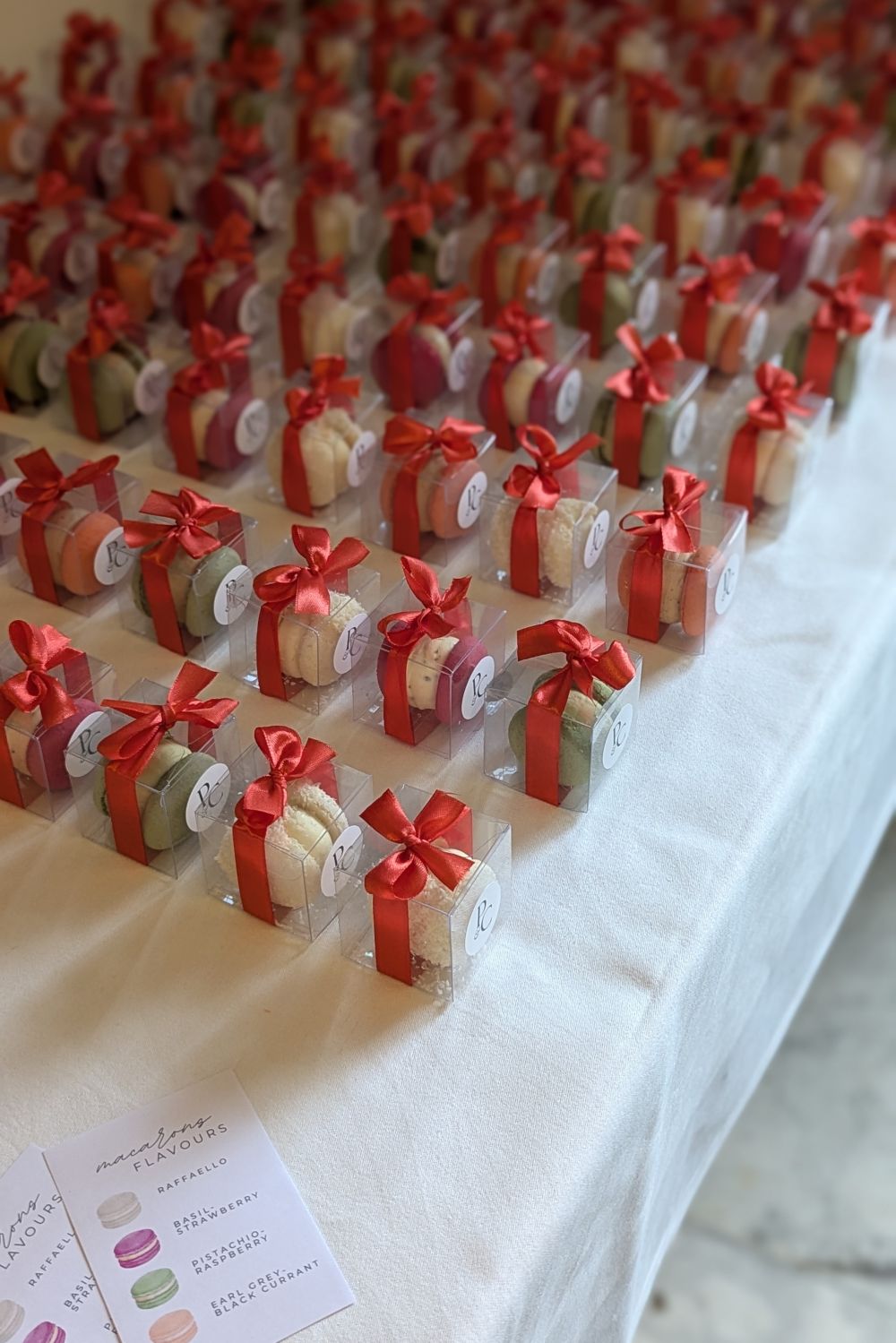 Rows of single boxed macarons, each closed with a red ribbon and a round monogram sticker