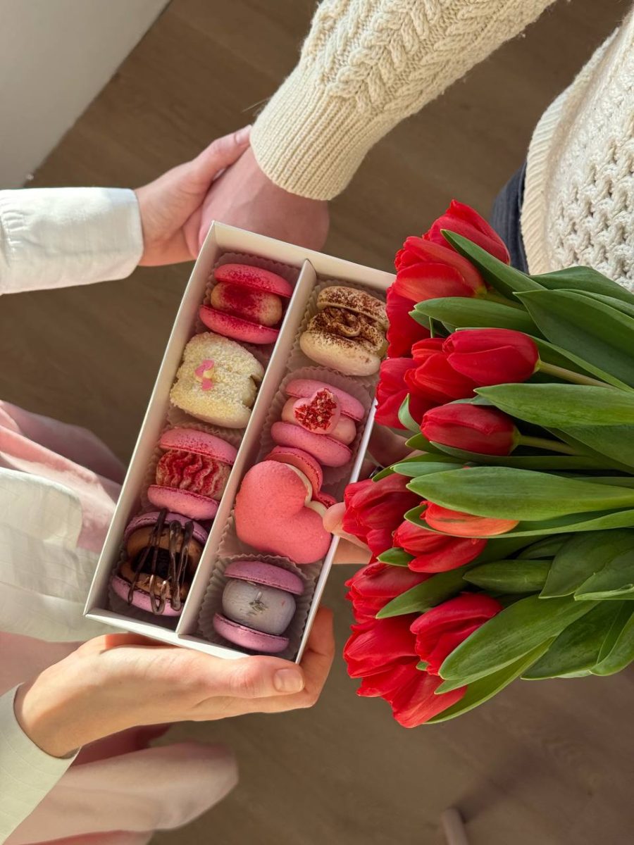 Hands passing a box of colourful macarons next to a bunch of red tulips